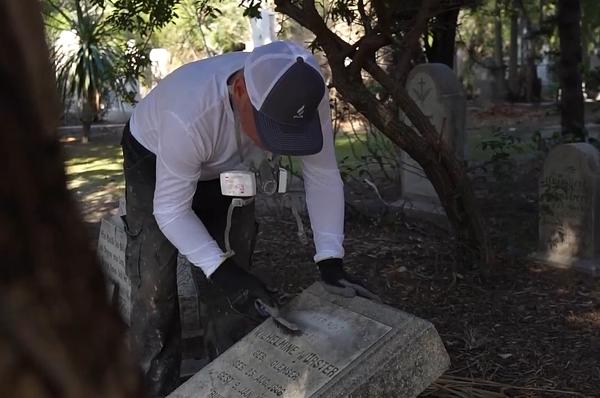 Tending professional safely cleaning a granite monument in compliance with cemetery rules.