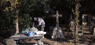 A Tending employee restores a cross-shaped monument that was broken in half